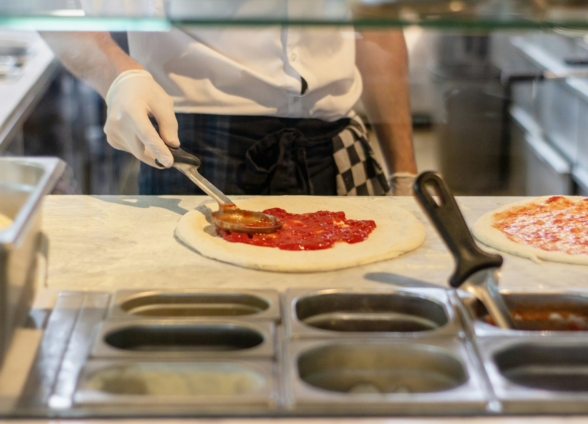 Pizzaiolo garnissant des pizzas devant un poste réfrigéré