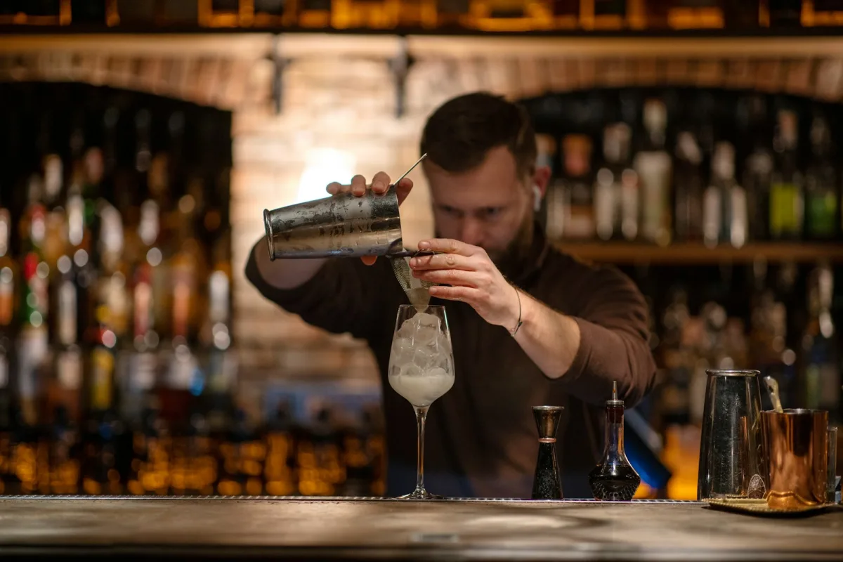 Bartender professionnel préparant des cocktails derrière le comptoir d'un bar animé — service CHR intensif